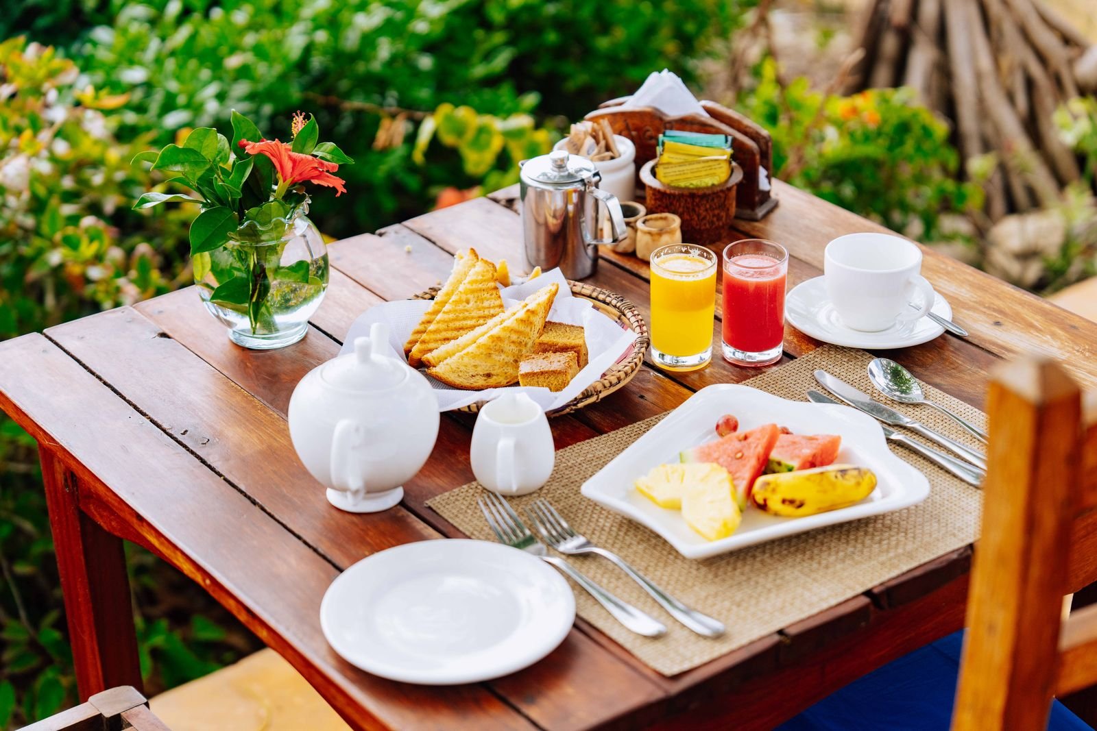 Breakfast with tropical fruit, toast and fresh juices on a wooden table in the garden