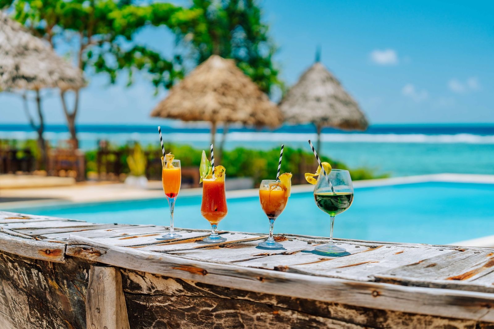 Tropical cocktails on the edge of the pool with thatched umbrellas and the sea behind